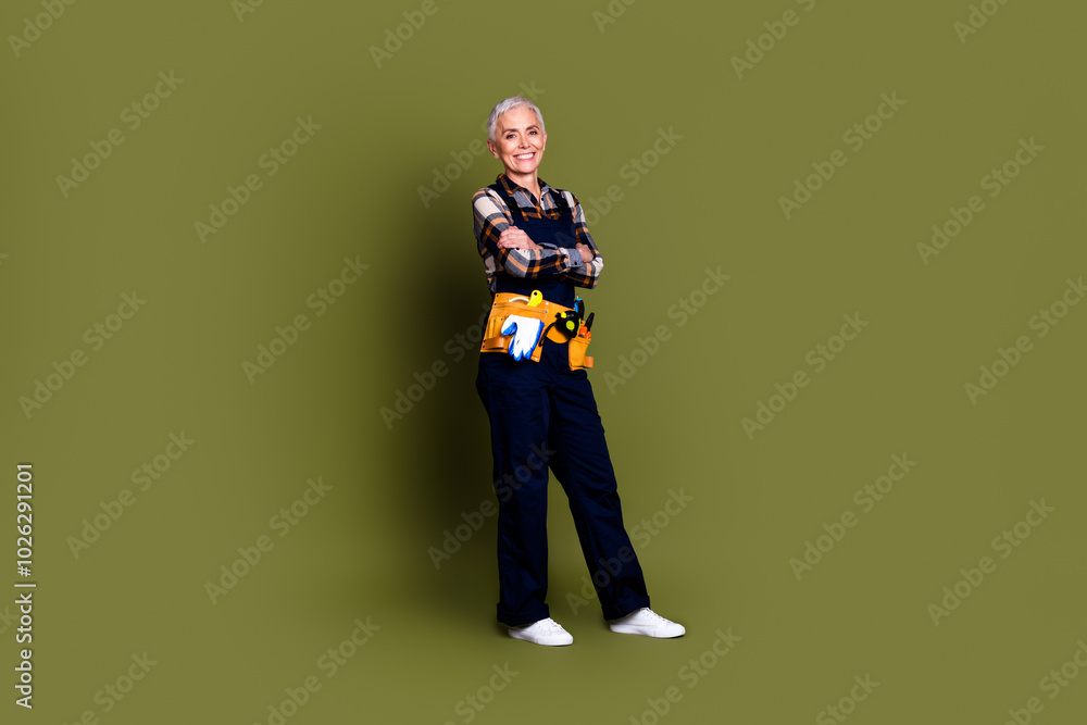Fototapeta premium Full size photo of senior female professional expert handyman crossed hands wear blue workwear overall isolated on khaki color background
