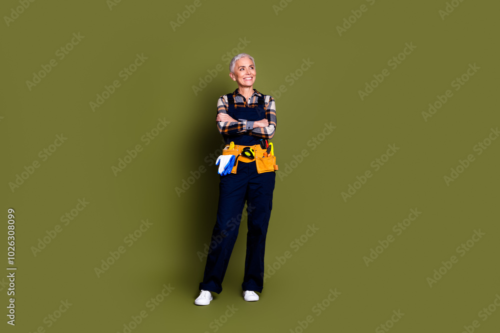 Fototapeta premium Full length photo of pensioner lady engineer crossed arms look empty space dressed blue workwear overall isolated on khaki color background