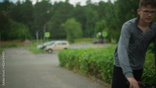 Wallpaper Mural Young boy wearing glasses rides bicycle on interlock path, surrounded by greenery, parked cars, pedestrians, signpost in background, quiet suburban street, with greenery in the background Torontodigital.ca