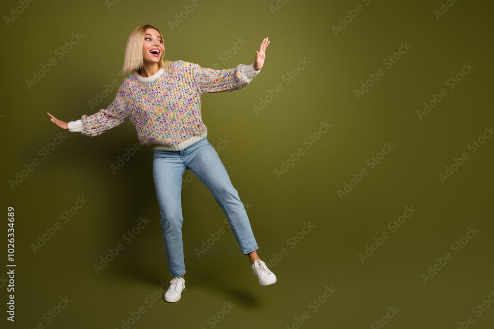 Cheerful young woman in colorful knit sweater posing playfully against khaki background, expressing excitement and joy Cheerful young woman in colorful knit sweater posing playfully against khaki background, expressing excitement and joy