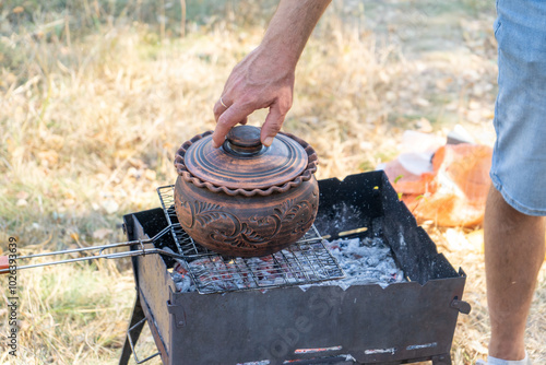 Clay pot with food on the grill. Cooking food on a fire outside. Camping outdoor. Sheff hand photo