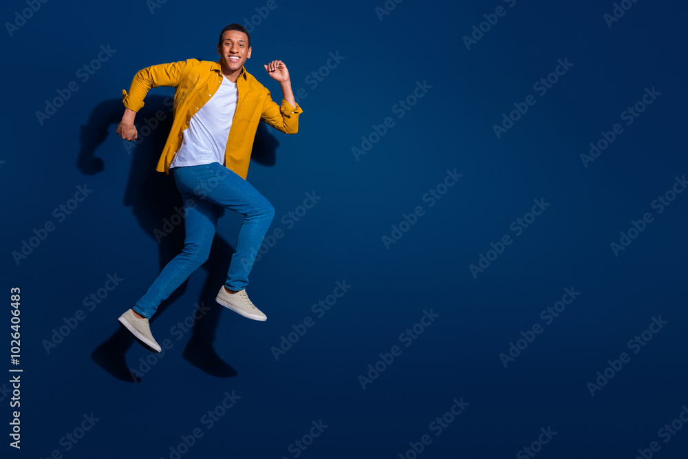 Obraz premium Full body length photo of attractive sporty man short hair wearing jeans and shirt running fast isolated on dark blue color background