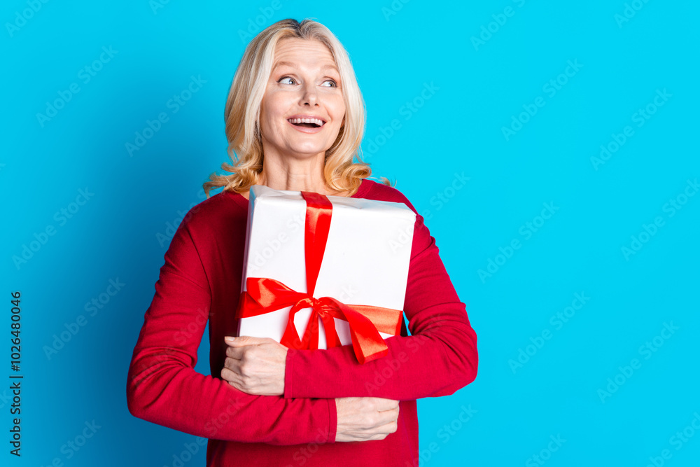 Photo portrait of pretty senior female look empty space hold giftbox wear trendy red outfit isolated on blue color background Photo portrait of pretty senior female look empty space hold giftbox wear trendy red outfit isolated on blue color background