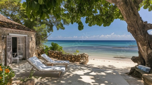 Two wooden lounge chairs on a sandy beach with a clear view of the ocean and lush green hills in the distance.