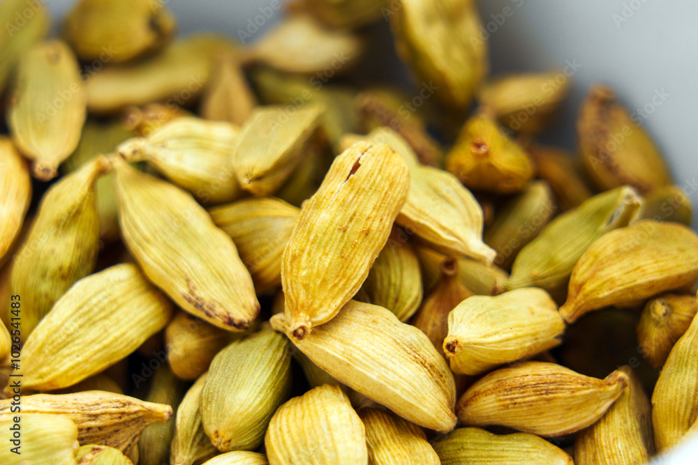Fototapeta premium Dried aromatic cardamon pods fill white bowl. Macro shot. Green cardamom spice