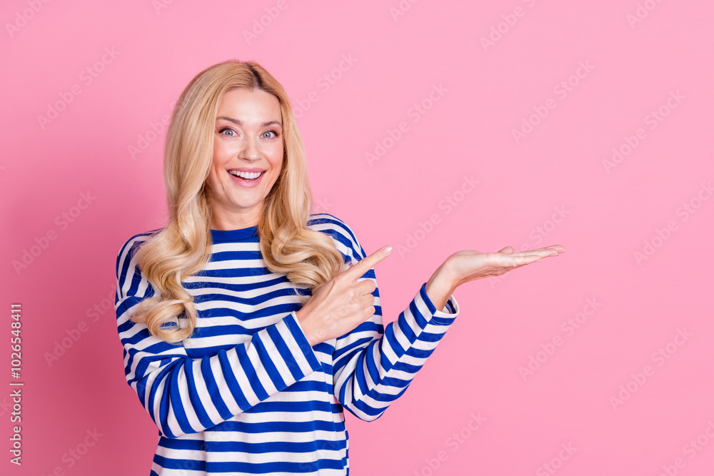 Photo of cheerful glad cute woman wear stylish striped clothes hold empty space isolated on pink color background Photo of cheerful glad cute woman wear stylish striped clothes hold empty space isolated on pink color background