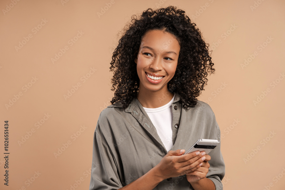 © Maria Vitkovska - Smiling African American woman holding mobile phone looking to the side in studio