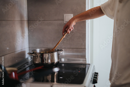 A person stirs pasta in a pot on a modern stove, showcasing home cooking and culinary skills in a cozy kitchen setting.