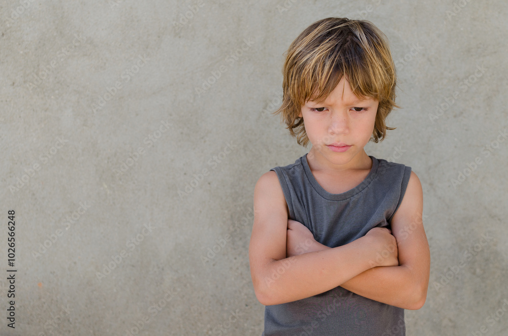 Horizontal portrait of upset and angry caucasian blond kid standing with crossed arms and looking down over grey background. Family relations, social and psychologies issues concepts. Copy space. Horizontal portrait of upset and angry caucasian blond kid standing with crossed arms and looking down over grey background. Family relations, social and psychologies issues concepts. Copy space.