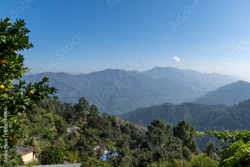 A serene mountain landscape with lush green hills, scattered village homes and clear blue sky.Natural beauty and tranquility of rural life in the Himalayas. Perfect for nature and outdoor exploration.