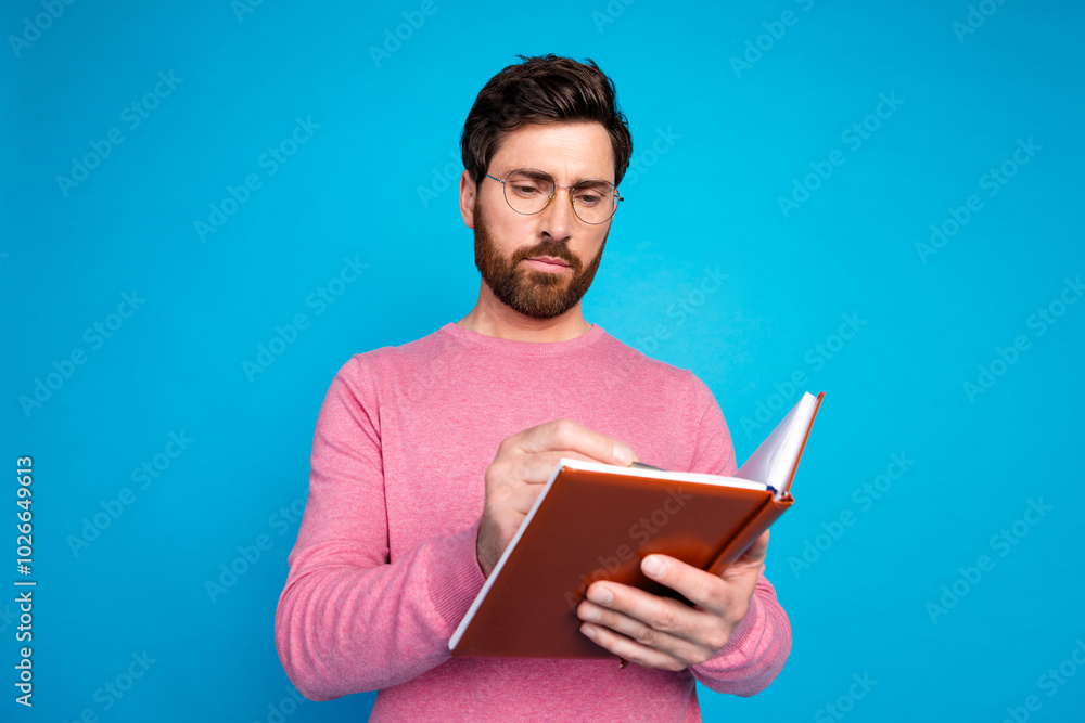 Thoughtful bearded man in pink sweater reading a book against blue background for business and education concepts Thoughtful bearded man in pink sweater reading a book against blue background for business and education concepts