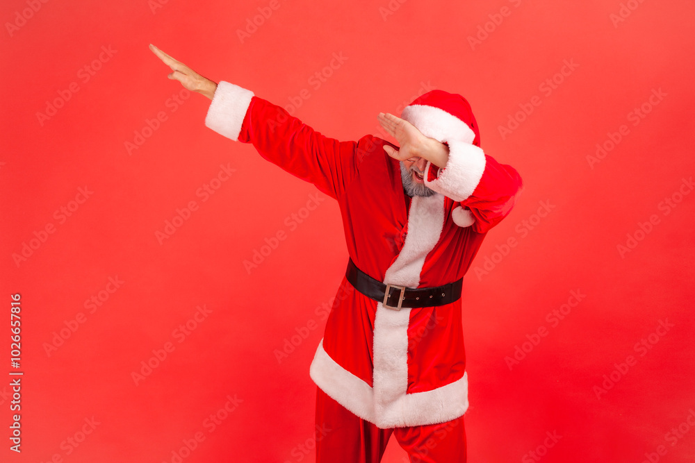 Internet trend. Portrait of man wearing santa claus costume and red hat showing dab dance move, celebrating, performing dabbing youth trends. Indoor studio shot isolated on red background. Internet trend. Portrait of man wearing santa claus costume and red hat showing dab dance move, celebrating, performing dabbing youth trends. Indoor studio shot isolated on red background.