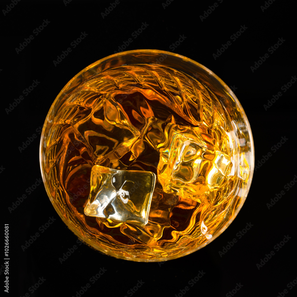 Glass of whiskey with ice cubes on black background. As whiskey is poured from the bottle into the glass Glass of whiskey with ice cubes on black background. As whiskey is poured from the bottle into the glass