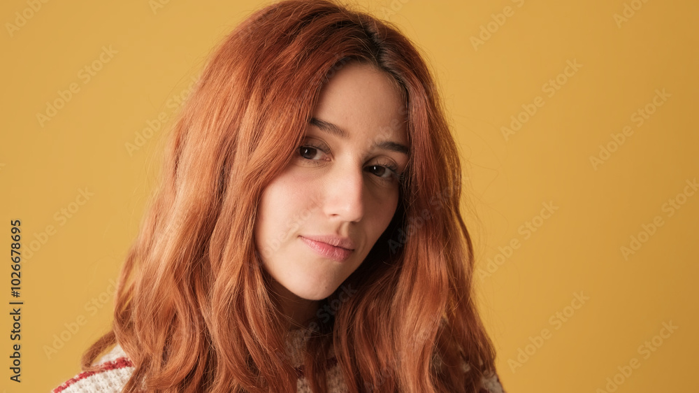 Close-up of smiling red-haired girl looking at camera in studio on yellow background Close-up of smiling red-haired girl looking at camera in studio on yellow background