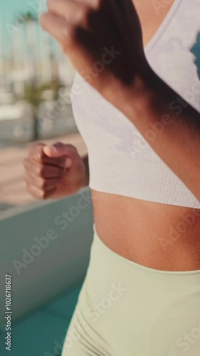 Close-up of a fit girl in sportswear doing street workout, running along the sea, focus on body and arms