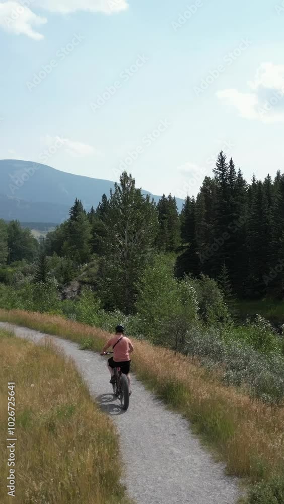 A man bikes down a path in a sunny valley. He is riding a fat tire bike. Enjoy the view of the trees and mountains. Crowsnest Pass, Alberta, Canada. A man bikes down a path in a sunny valley. He is riding a fat tire bike. Enjoy the view of the trees and mountains. Crowsnest Pass, Alberta, Canada.