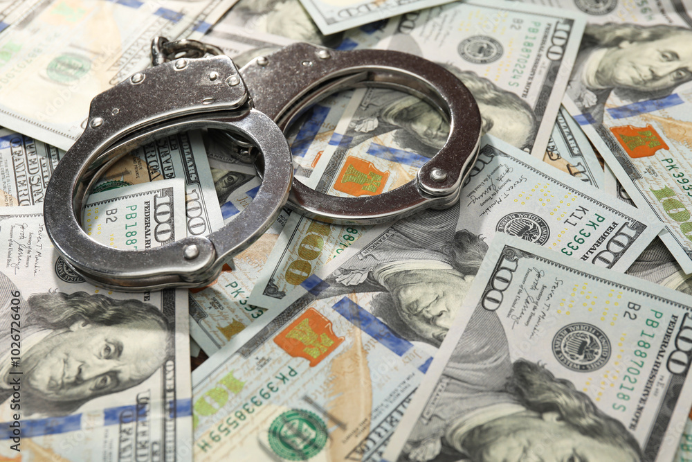 Handcuffs on pile of dollar banknotes, closeup Handcuffs on pile of dollar banknotes, closeup