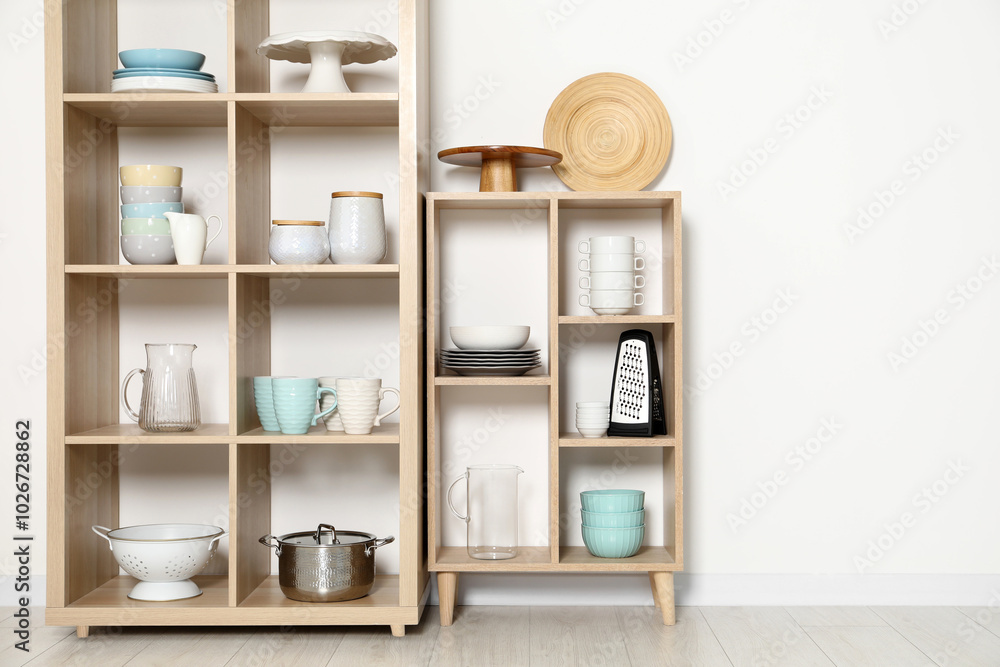 Wooden shelving units with kitchenware near white wall indoors Wooden shelving units with kitchenware near white wall indoors
