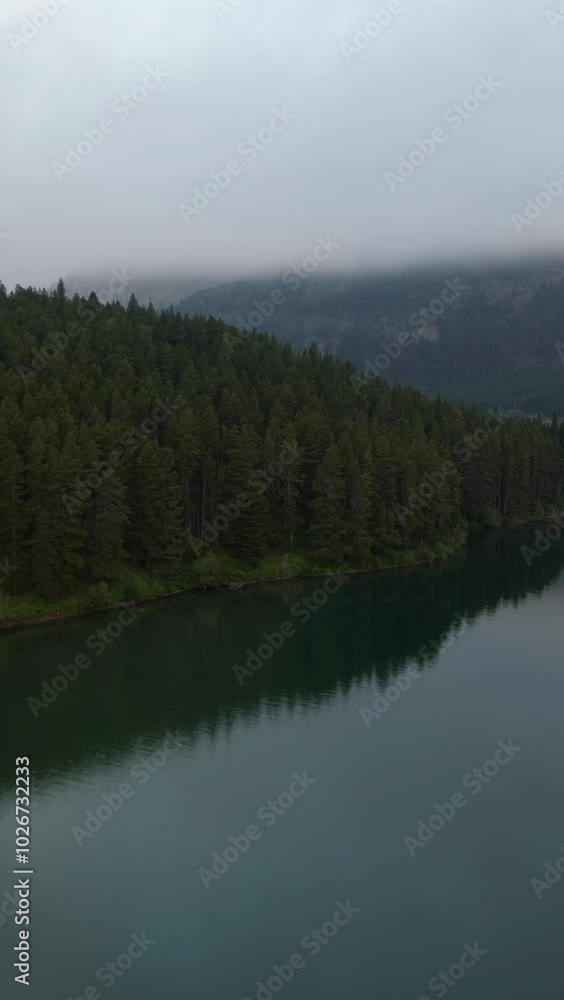 Aerial view of a misty lake surrounded by pine trees and mountains. Crowsnest Pass, Alberta, Canada. Aerial view of a misty lake surrounded by pine trees and mountains. Crowsnest Pass, Alberta, Canada.