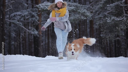 Happy girl run with border collie dog in snowy winter forest in slow motion. Merry Christmas New year Day. Cheerful puppy jump to owner. Friendship of girl and pet. Having fun together. Dogs best