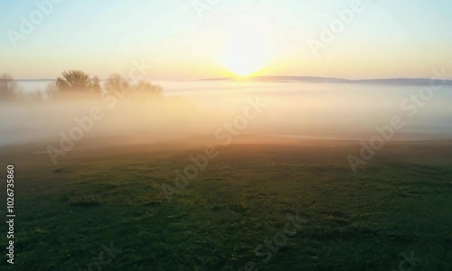 shot with morning fog lifting: The camera starts close to the fog-covered ground, capturing the fog lifting, then rises to reveal the clear morning sky emerging.