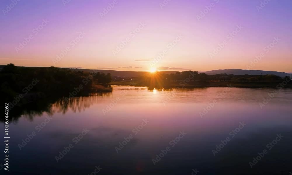 Dolly shot with sunrise reflection: The camera starts close to a calm body of water reflecting the sunrise, then dollies back to show the sky's changing colors and the surrounding landscape. Dolly shot with sunrise reflection: The camera starts close to a calm body of water reflecting the sunrise, then dollies back to show the sky's changing colors and the surrounding landscape.
