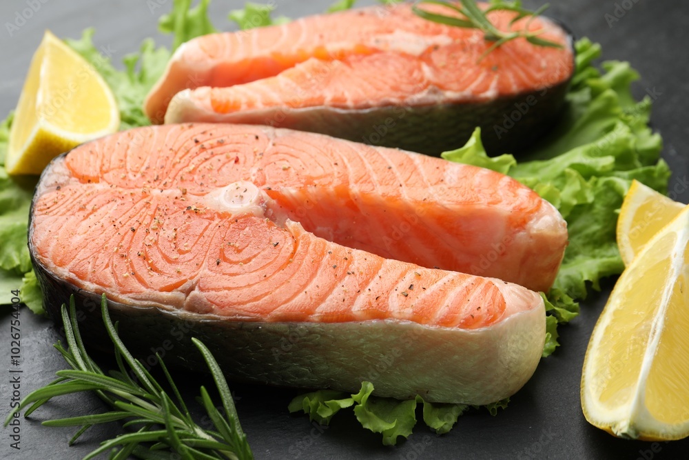Fresh raw salmon steaks with spices, lemon, lettuce and rosemary on dark table, closeup Fresh raw salmon steaks with spices, lemon, lettuce and rosemary on dark table, closeup