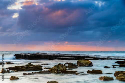 Moody sunrise seascape with clouds and casscades over the rock platorm at the rocky inlet photo