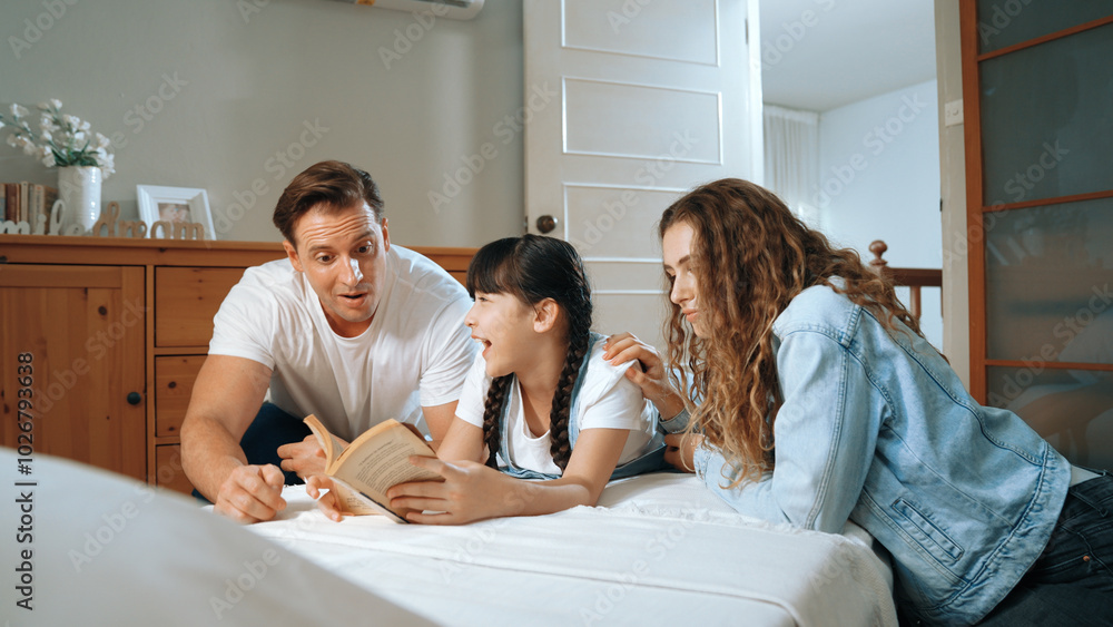 Bedtime story with childhood storytelling, mom and dad reading a fantasy book together to their little young girl in cozy and comfortable bedroom. Modern family happy time. Synchronos Bedtime story with childhood storytelling, mom and dad reading a fantasy book together to their little young girl in cozy and comfortable bedroom. Modern family happy time. Synchronos