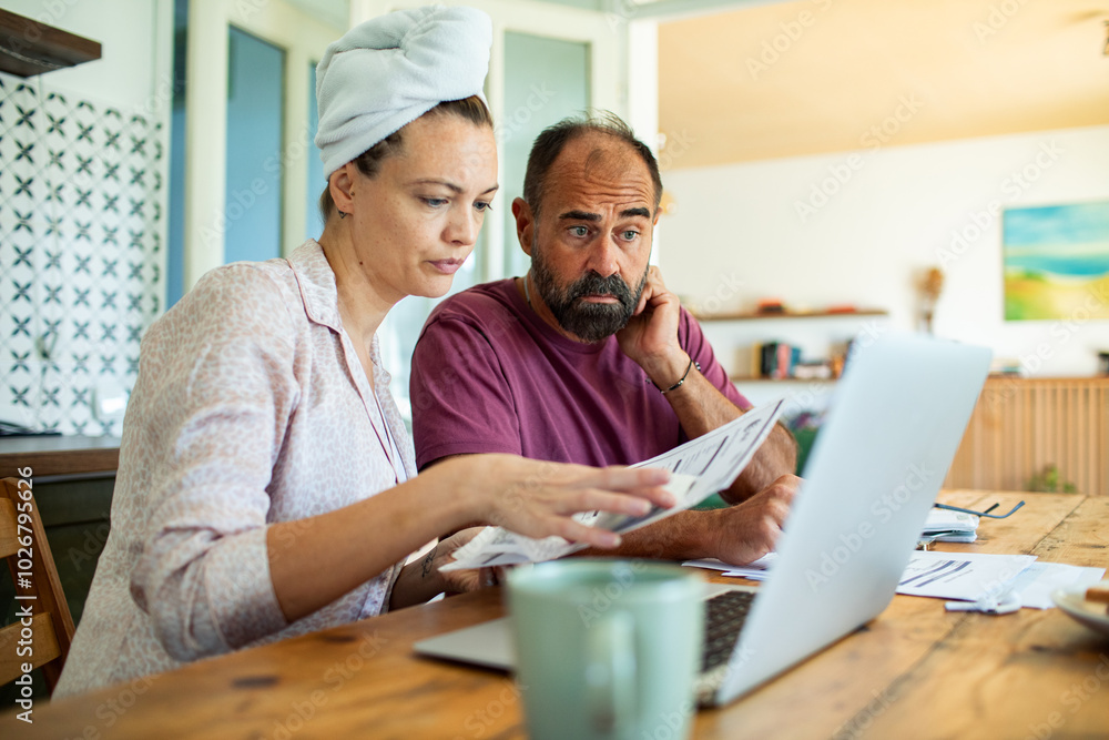Fototapeta premium Couple reviewing bills together at home with laptop in kitchen