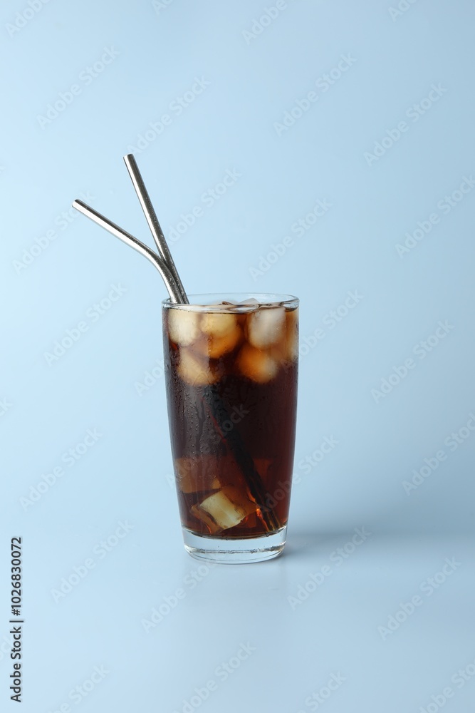 Tasty refreshing drink with straws in glass on light blue background Tasty refreshing drink with straws in glass on light blue background