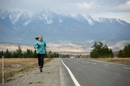 Sports girl is engaged in jogging on the highway against the background of mountains