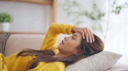 Asian woman resting at home on couch, feeling exhausted after work, lacking energy, or overworked, too tired, and lacking motivation