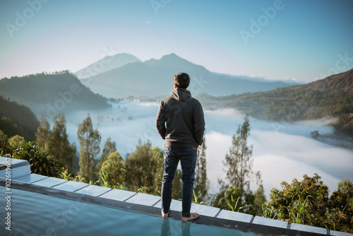 A man is standing confidently on a ledge while admiring the breathtaking view of a beautiful lake surrounded by majestic mountains