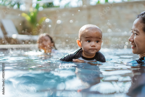 A joyful woman is happily holding a baby in a swimming pool, creating a lovely moment filled with fun and laughter in the water photo