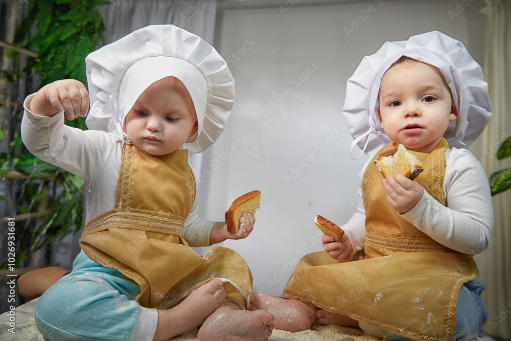 Two toddlers dressed as chefs delight in a playful baking session, surrounded by flour and treats, sharing laughter and joy
