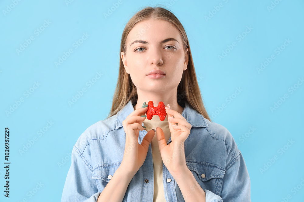 Young woman with thyroid gland model on blue background Young woman with thyroid gland model on blue background