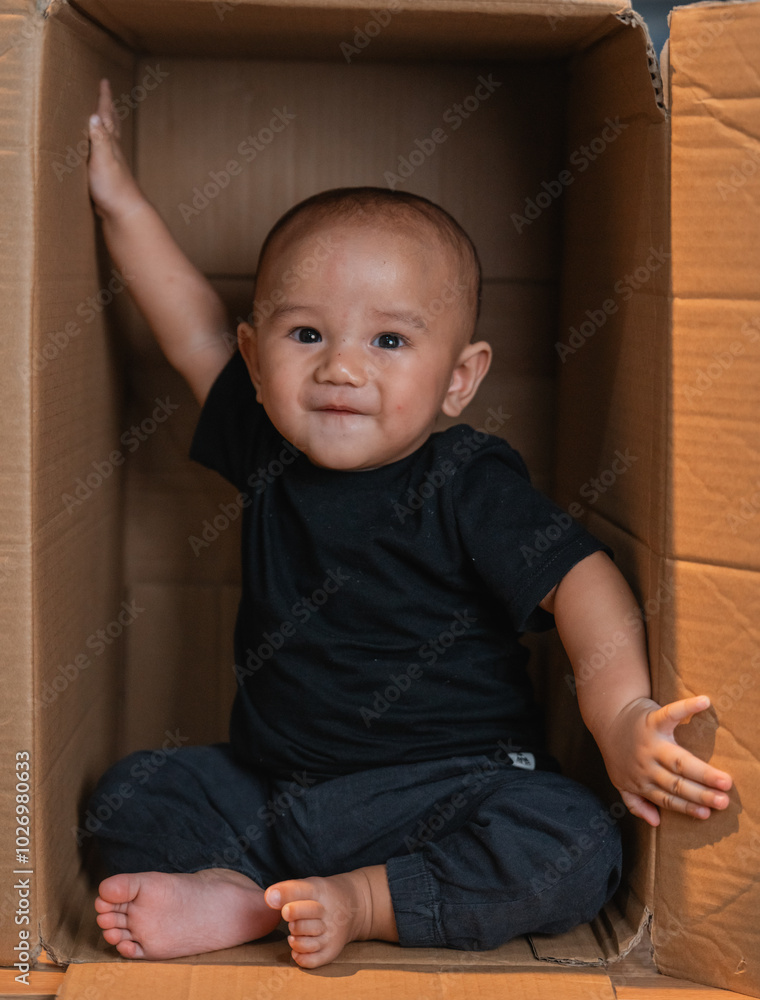 Fototapeta premium A cheerful baby in a cardboard box reaches out joyfully, capturing childhood and exploration