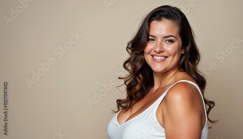 A young woman with long, curly brown hair wearing a white tank top, smiling at the camera