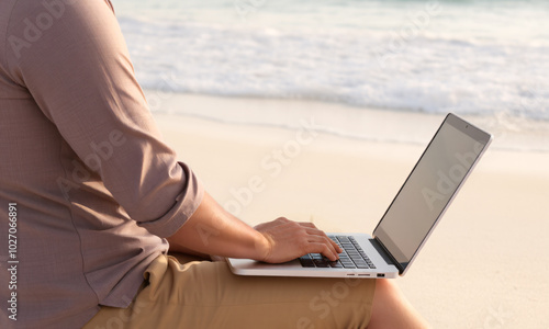 a businessman sitting on the beach with his laptop open on his knees photo