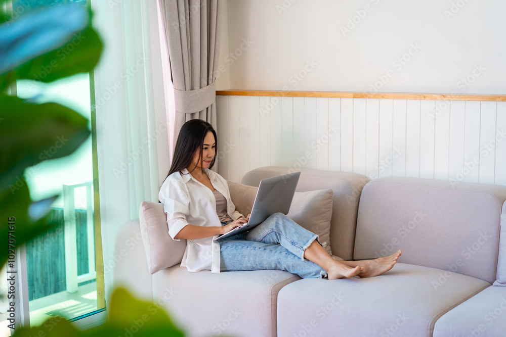 Young Asian female relaxing and using laptop on a sofa at home Young Asian female relaxing and using laptop on a sofa at home