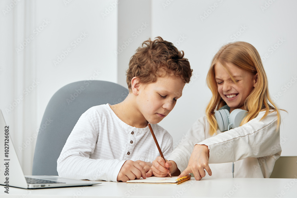 Happy children studying together at home using laptops and headphones for online education The two siblings, a boy and a girl, are sitting at a table in the living room, focused and engaged in their Happy children studying together at home using laptops and headphones for online education The two siblings, a boy and a girl, are sitting at a table in the living room, focused and engaged in their