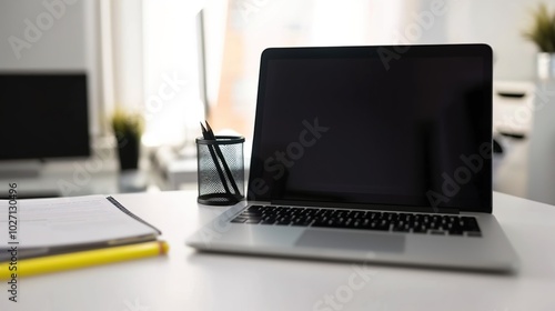 Front view laptop on white table. There is paper and a pen holder nearby. In modern office space