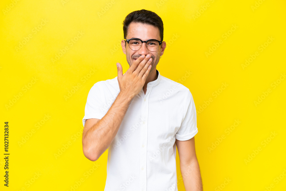 Young handsome man over isolated yellow background happy and smiling covering mouth with hand Young handsome man over isolated yellow background happy and smiling covering mouth with hand