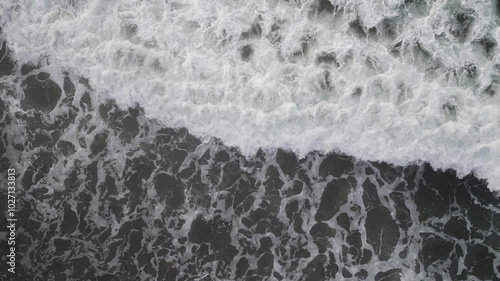 An Aerial view of White top waves crashing over rocks on the shoreline