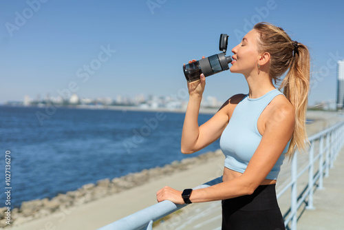 Sport woman jogger runner drinking water from bottle at city embankment river closeup