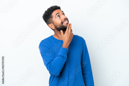 Young Brazilian man isolated on white background looking up while smiling