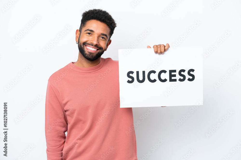 Young Brazilian man isolated on white background holding a placard with text SUCCESS with happy expression Young Brazilian man isolated on white background holding a placard with text SUCCESS with happy expression