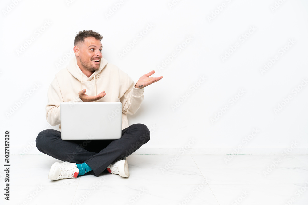 Young caucasian man with a laptop sitting on the floor isolated on white background with surprise facial expression Young caucasian man with a laptop sitting on the floor isolated on white background with surprise facial expression