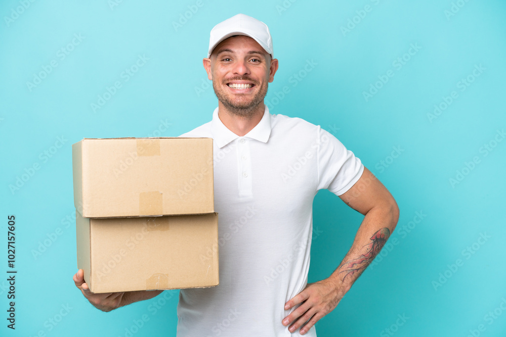 Delivery caucasian man isolated on blue background posing with arms at hip and smiling Delivery caucasian man isolated on blue background posing with arms at hip and smiling